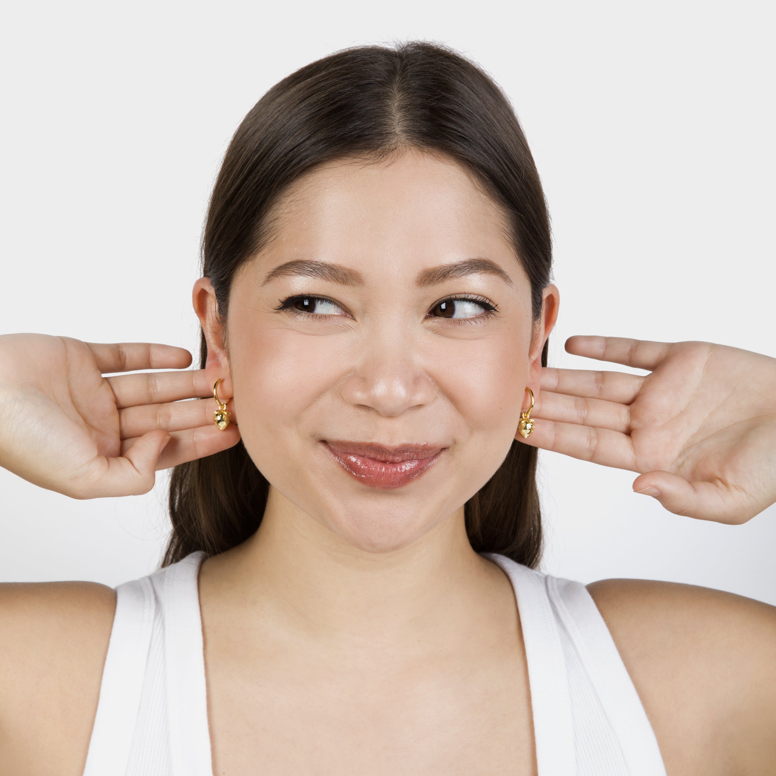 Model smiling with hands pressed to ears, showing off gold strawberry earrings.