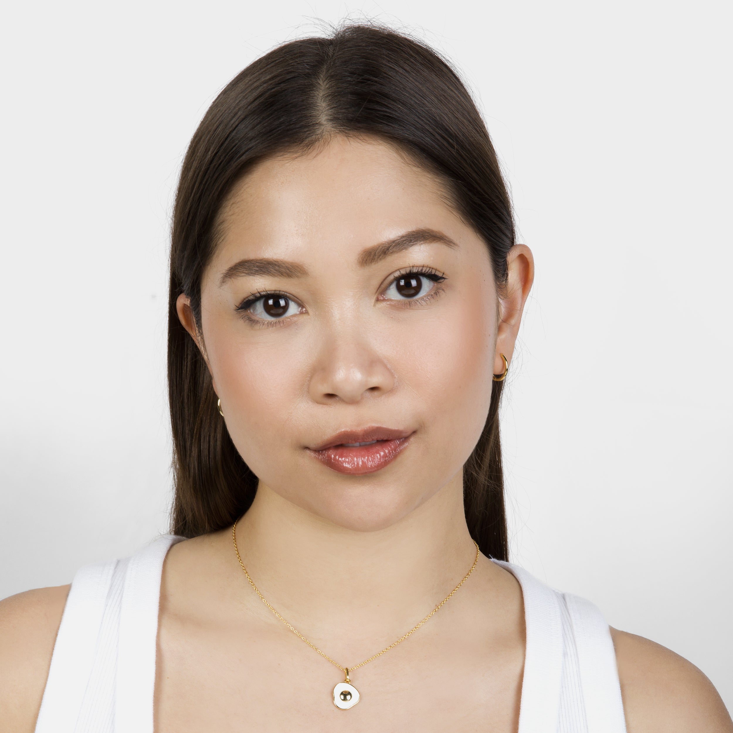 Model wearing a sunny-side up egg necklace with a glossy gold yolk and white egg white pendant on a gold chain, styled against a neutral background.