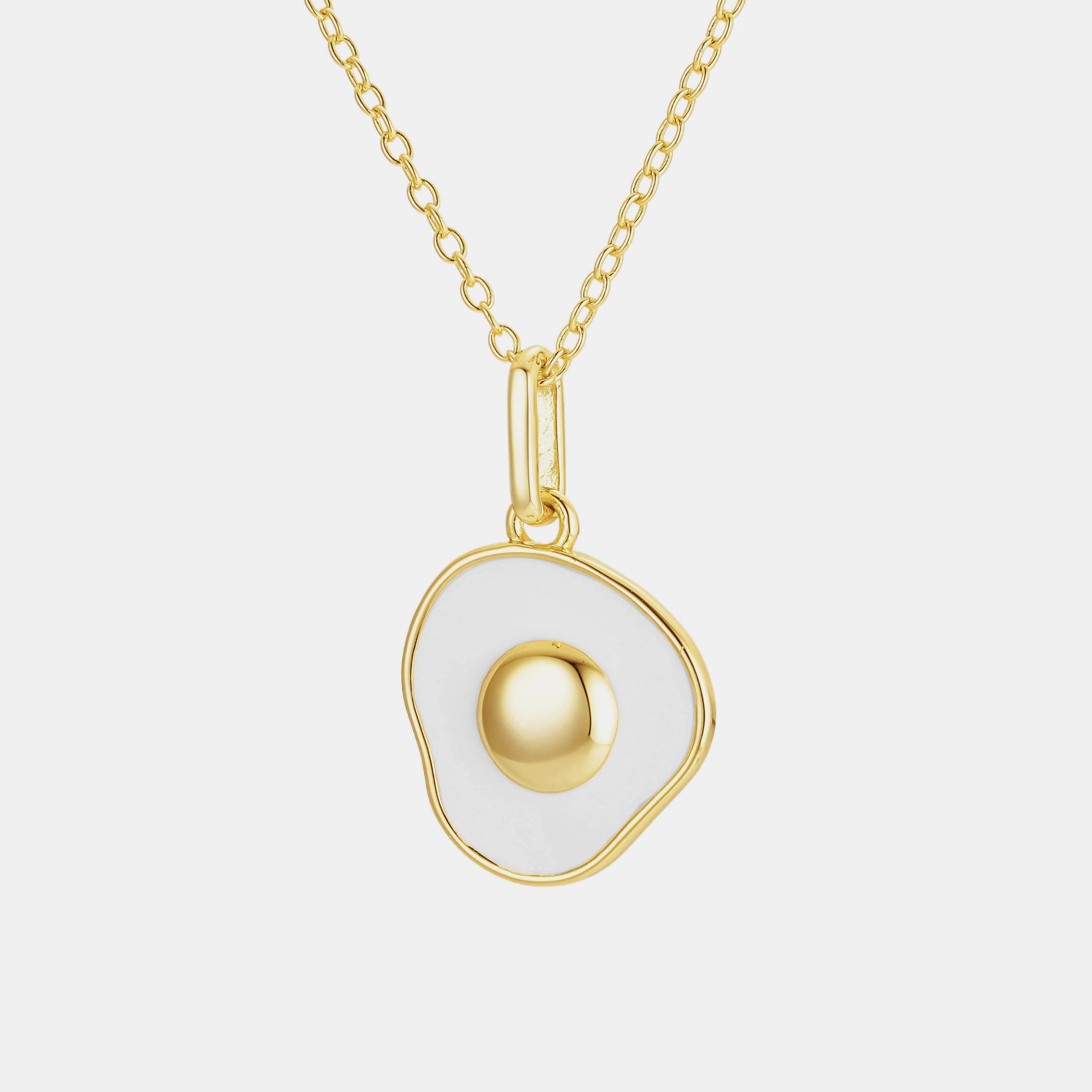 Sunny-side up egg necklace with a glossy gold yolk and white egg white pendant, on a gold chain, displayed on a clean white background.