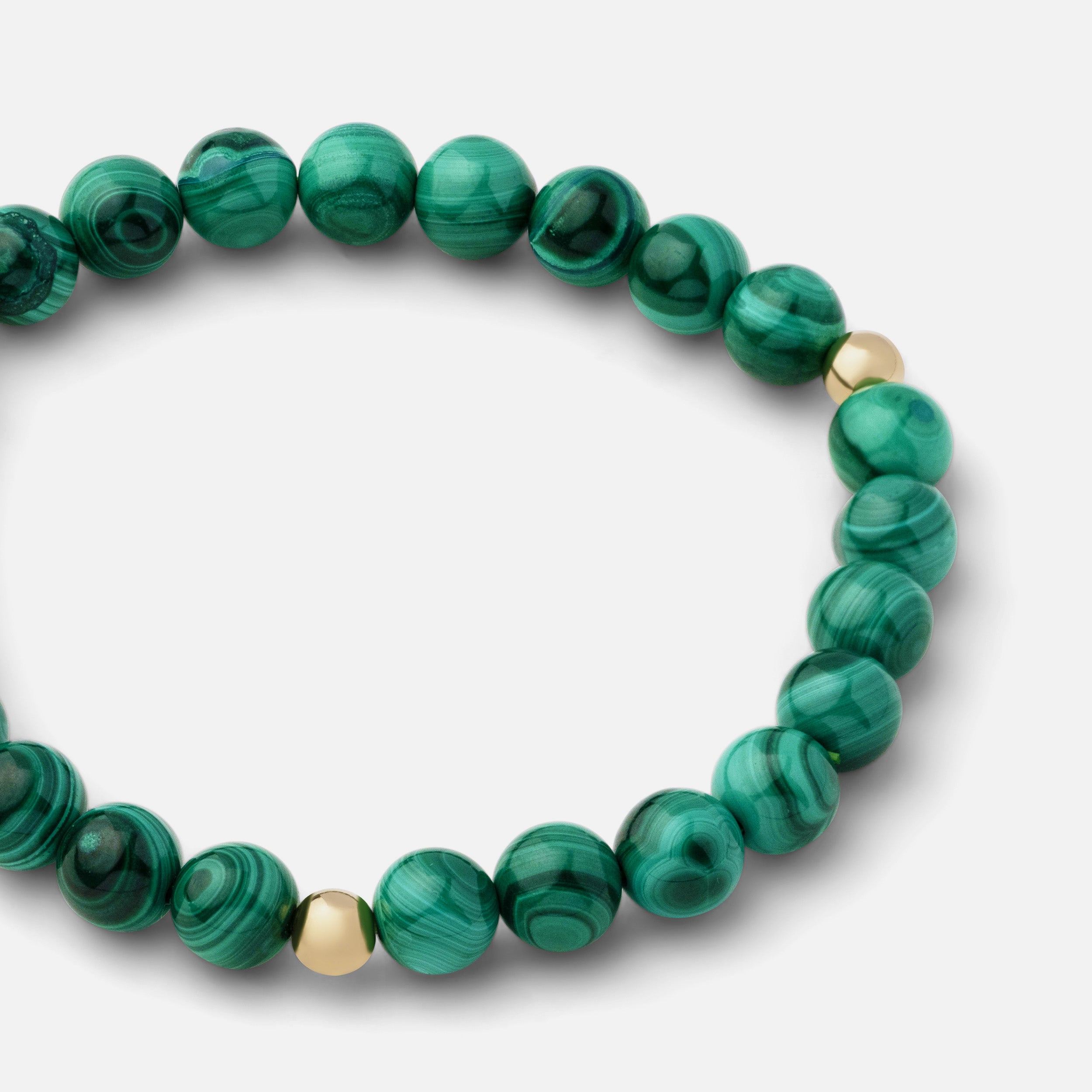 Close-up of a rich green malachite bracelet showcasing beautiful banding and plume-like patterns, ideal for wearing solo or with other gold jewelry.