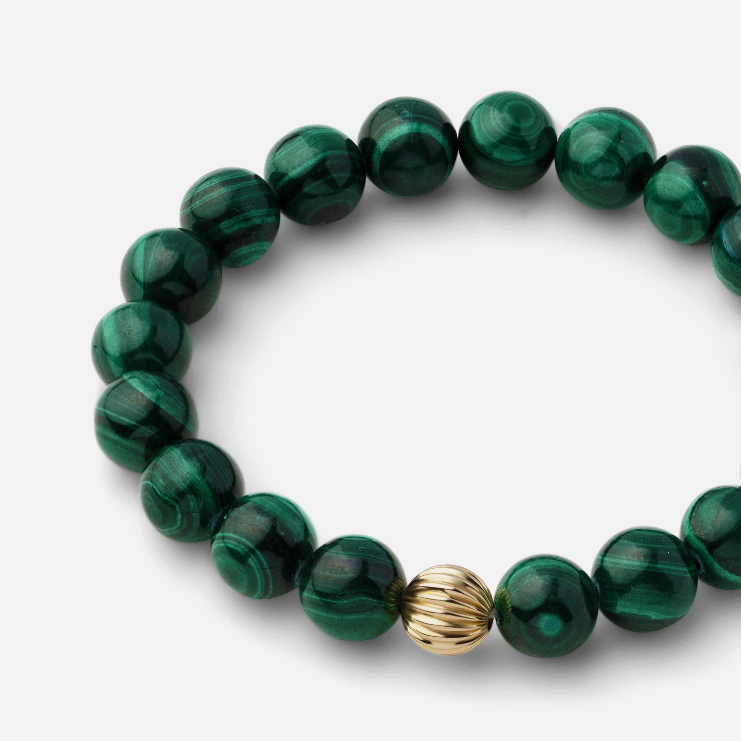 Close-up of a rich green malachite bracelet showcasing beautiful banding and plume-like patterns, ideal for wearing alone or with other gold jewelry pieces.