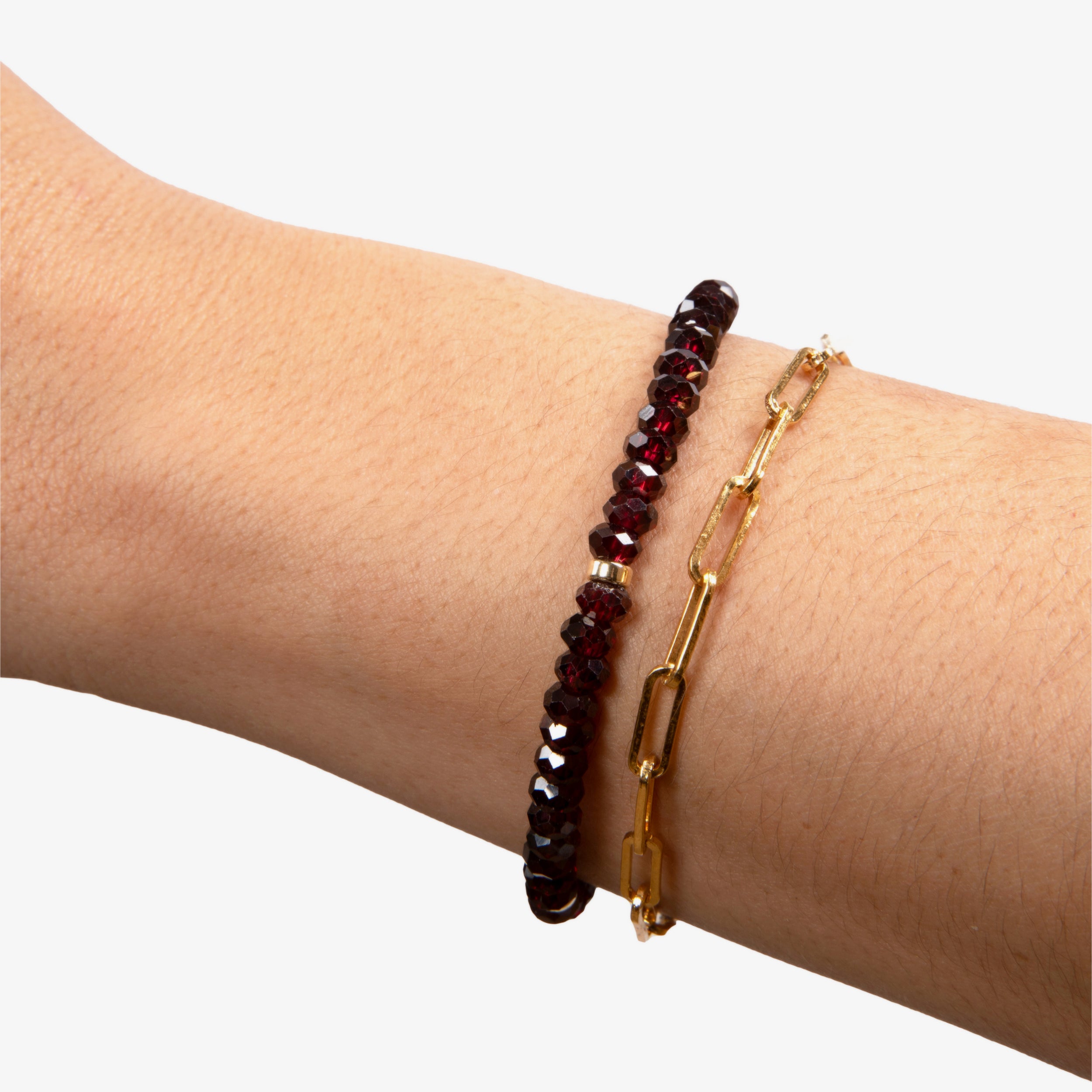 Close-up of a model's wrist wearing a blood red garnet bracelet stacked with a paperclip bracelet, demonstrating the versatile and elegant style.