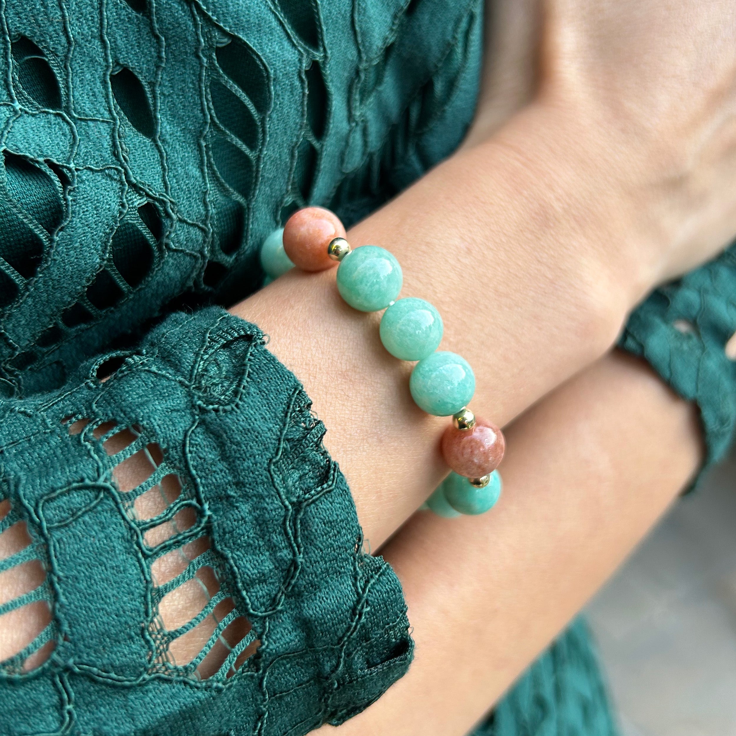 Close-up of a model's wrist with hands crossed, showcasing a bracelet featuring the stunning ocean blue color of ice amazonite paired with sparkled sunstones, perfect for a day-to-night style.