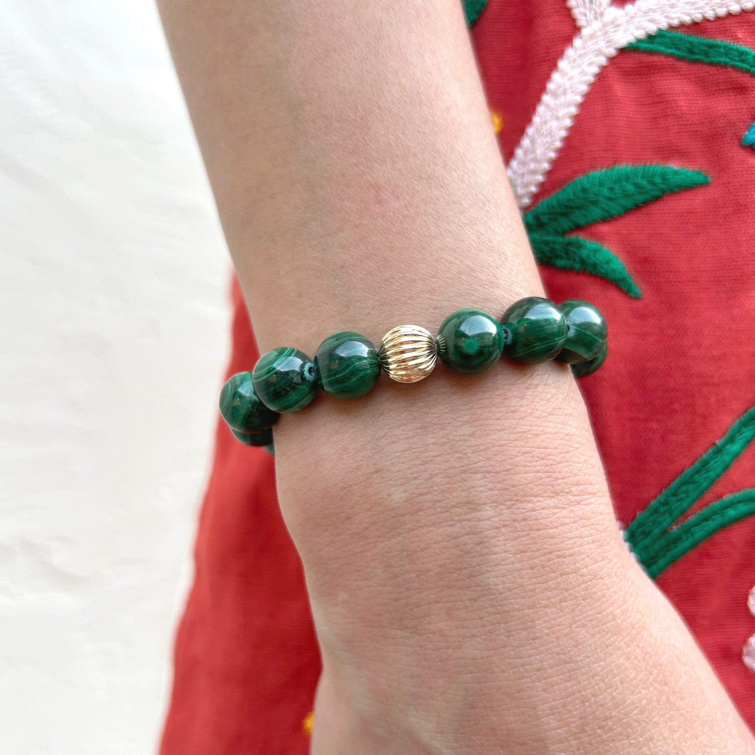 Close-up of a model's wrist wearing a rich green malachite bracelet, highlighting its beautiful banding and plume-like patterns, paired with other gold jewelry pieces.