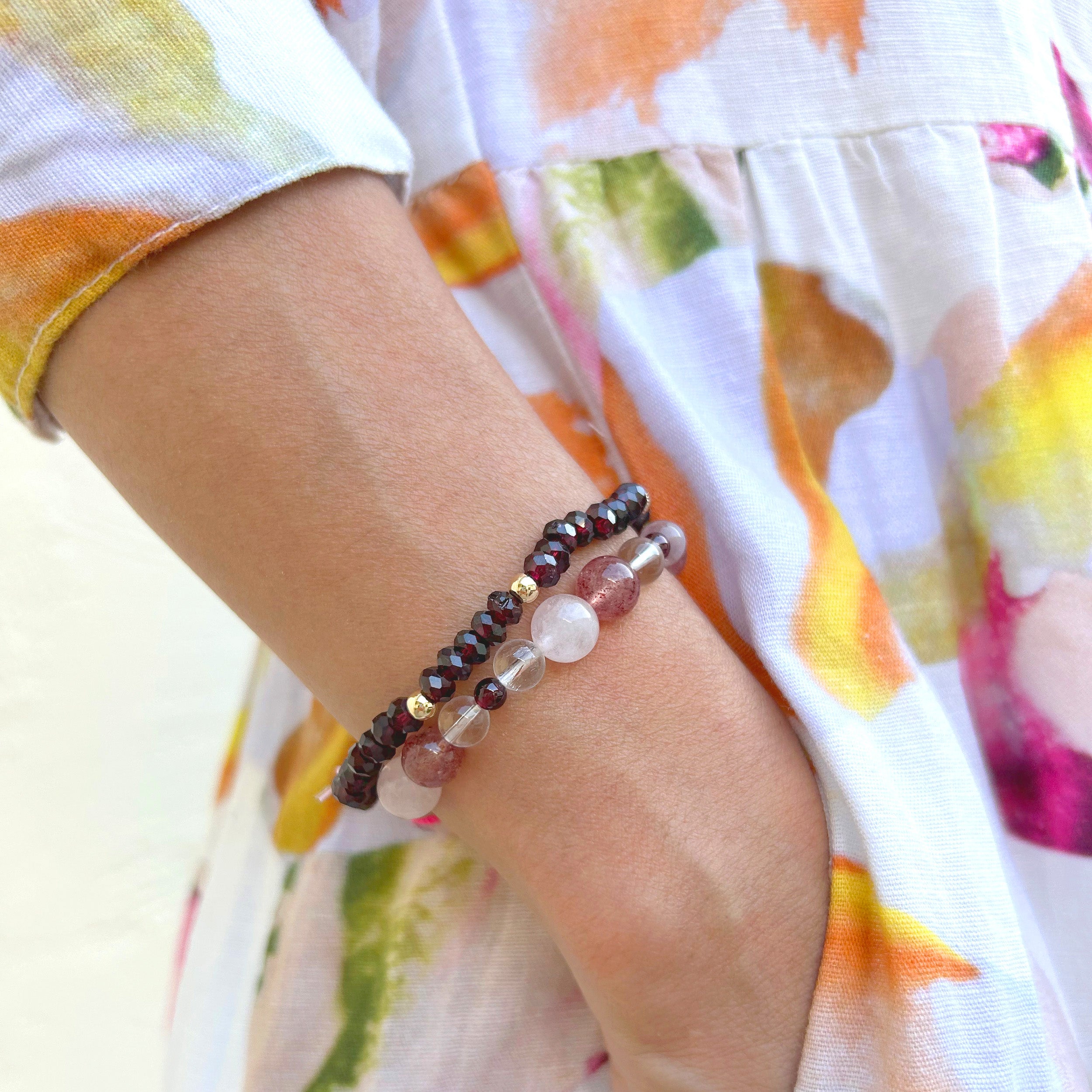 Close-up of a model's wrist wearing a bracelet with red strawberry quartz, blood red garnet, light pink rose quartz, and clear quartz accents, with the model's hand in a dress pocket.